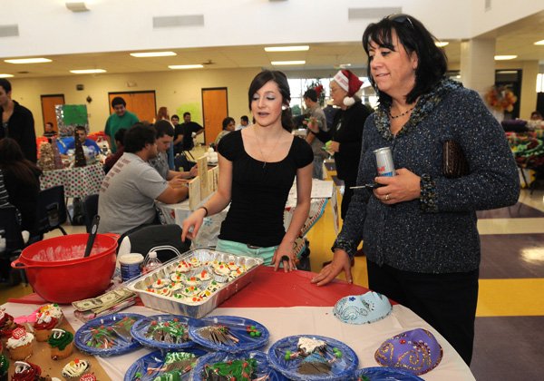 Student Erica Estrada, left, shows Karen Steen, Heritage High School principal, some of the baked goods for sale on Thursday at the “Simply Bazaar” event in Rogers. 