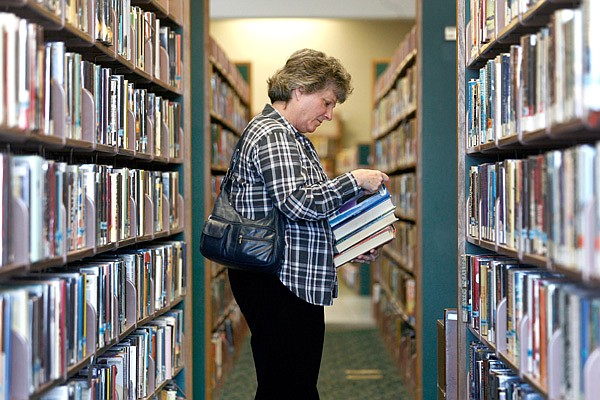 Diana Ashley of Rogers peruses through shelved books Wednesday at the Rogers Public Library. Area librarians say e-books and other electronic media are flying off virtual shelves. 