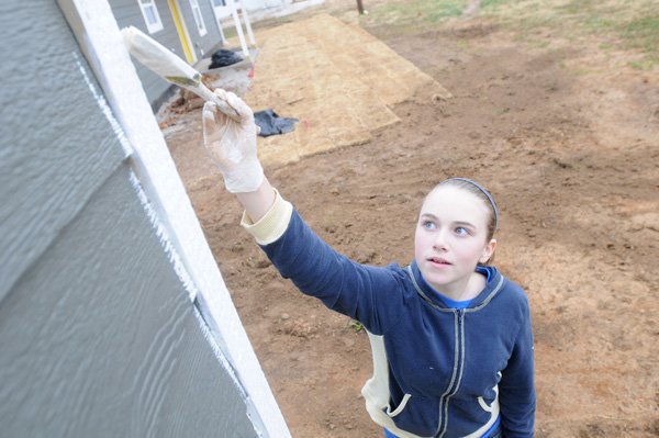 Mady Gray, 12, reaches up as far as she can Saturday while painting the trim on the storage shed next to a new house built by Habitat for Humanity of Washington County at 100 Terry Ave. in Springdale. About a dozen student volunteers helped with the house after researching the organization for a school project. Mady said she chose Habitat for Humanity because it “benefits people around the world.” The house’s dedication ceremony is scheduled for 2 p.m. today. 