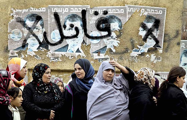 Egyptian women wait to vote Saturday in Cairo under posters of President Mohammed Morsi defaced with the word “killer.” 