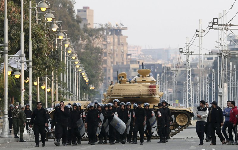 Egyptian riot police walk past a military tank guarding the presidential palace in Cairo, Egypt, Sunday, Dec. 16, 2012. Key Egyptian rights groups called Sunday for a repeat of the first round of the constitutional referendum, alleging the vote was marred by widespread violations. Islamists who back the disputed charter claimed they were in the lead with a majority of “yes” votes.