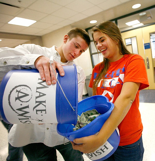 Stokes Wenzler, Deca vice president, dumps donated money into the bucket Friday held by club president Meredith Breach, both seniors at Rogers High School. Club members held buckets in the school’s corridors to raise $1,000 in a minute. The donated money goes to the Make-A-Wish 