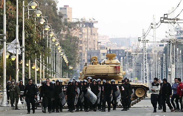 Egyptian riot police walk past a military tank guarding the presidential palace in Cairo on Sunday. Islamists claimed a constitutional referendum had 57 percent support in the first round of voting, in which rights groups claimed widespread violations.


