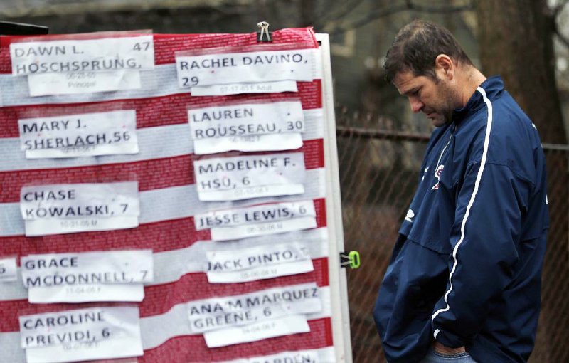 A man pays respects Monday in Newtown, Conn., near a U.S. flag with the names of victims on a makeshift memorial, including that of Jesse Lewis, whose grandfather David Lewis lives in Fayetteville.