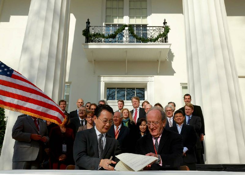 Eugene Yun (left), managing director of the P80 Group Foundation, and Carlos Westendorp, secretary-general of the Club de Madrid, sign the Little Rock Accord on Monday afternoon on the steps of the Old Statehouse. Supporters of the accord hope to persuade government-owned investment funds and other financial funds to back “sustainable growth” that is environmentally sensitive.