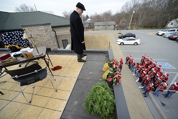 Michael Poore, superintendent of Bentonville Schools, listens Wednesday from the roof of the School District Administration Building as a group of students from Mary Mae Jones Elemetary School sing Christmas carols in Bentonville. Poore was making good on his promise to work on the building’s roof if the goal of filling his office with food donations for the Samaritan Community Center was met. 