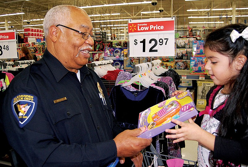 Alexander Police Chief Horace Walters looks over one of the Christmas gifts selected by Anyi Flores during the annual Shop With Our Cops night in Benton. Children who might not have had anything for Christmas were selected by their elementary-school teachers to go shopping with a Saline County law enforcement officer.
