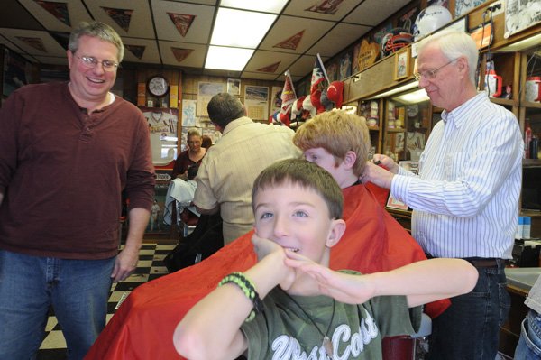 Ryan Howk, foreground, checks out his haircut Saturday after getting trimmed by barber Gary Townzen, right, during Townzen’s annual charity haircut day at Townzen Barber Shop to benefit Samaritan Community Center in Rogers. 