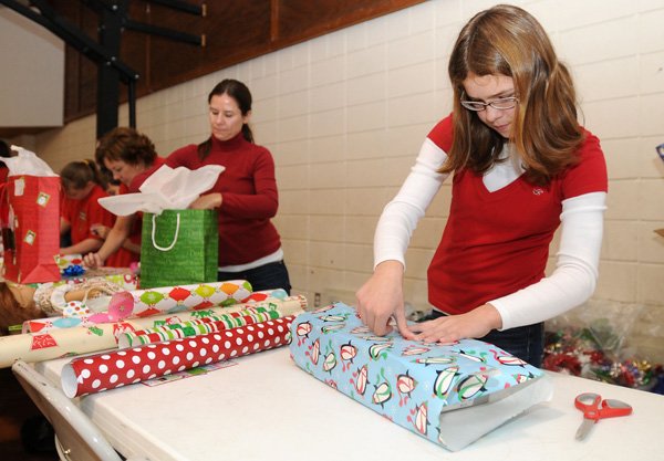 Lily Agnacian, 12, right, secures wrapping paper with a piece of tape Monday while wrapping presents alongside her mom, Jody Agnacian, left, during the fourth annual Miracle on 14th Street event at First Christian Church in Bentonville. The event provided free winter coats, toys, gift wrapping and a hot meal on a first come, first served basis. Last year, event organizers saw about 1,500 attendees and expected the same numbers this year. 