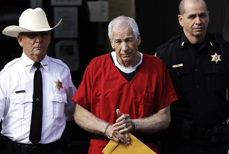 FILE - In this Oct. 9, 2012 file photo, former Penn State University assistant football coach Jerry Sandusky, center, is taken from the Centre County Courthouse by Centre County Sheriff Denny Nau, left, and a deputy, after being sentenced in Bellefonte, Pa. Sandusky was sentenced to at least 30 years in prison, effectively a life sentence, in the child sexual abuse scandal that brought shame to Penn State and led to coach Joe Paterno's downfall. The Sandusky saga was a top story in the sports world in 2012. (AP Photo/Matt Rourke, File)