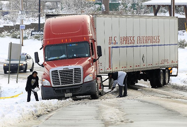 Truckers Michael Wells (left) and C’rone Hill try to dig snow and ice from underneath the wheels of their tractor-trailer Thursday morning after sliding off Kanis Road in Little Rock. 