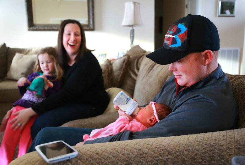 Katie Broadus (left) and daughter Avery, 4, watch as husband Joshua Broadus feeds their daughter London on the couch in their Benton home Sunday afternoon. Katie was forced to deliver London on the same couch early Wednesday morning by candlelight at the peak of bad road conditions and power failures caused by last week’s ice and snow. The ambulance sent for her ended up in a ditch, and the wrecker sent for the ambulance needed a wrecker. 