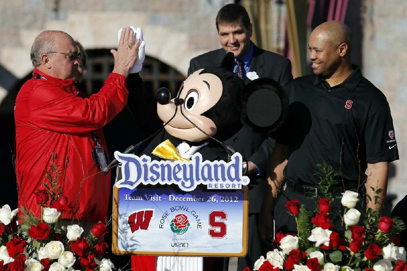Wisconsin Athletic Director Barry Alvarez (left) and a person dressed as Mickey Mouse, center, high-five as Stanford Coach David Shaw (right) watches during a news conference at Disneyland in Anaheim, Calif., Wednesday. Alvarez, who coached at Wisconsin from 1990-2005, will coach the Badgers in today’s Rose Bowl, following the departure of Bret Bielema to Arkansas. 