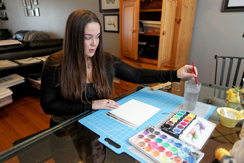 Kara Lunzer works on an abstract watercolor painting at a desk in her home. Lunzer sells her black and white watercolors on Etsy. 