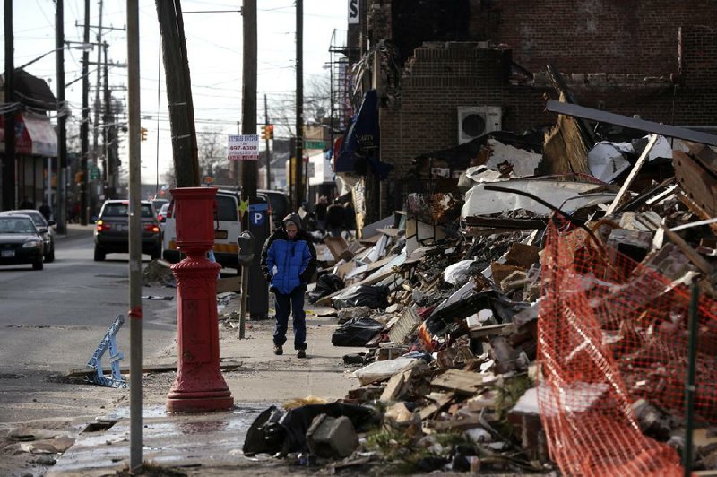 A pedestrian passes a commercial strip Wednesday in the Rockaways section of New York that burned down during superstorm Sandy. Insurer Munich Re AG estimated Thursday that the storm will lead to insurance payouts of $25 billion. 