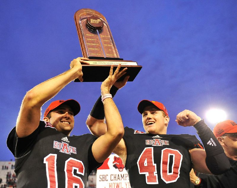 Arkansas State quarterback Ryan Aplin (left) hoists the Sun Belt Conference championship trophy with teammate Nathan Herrold on Dec 1. Aplin has remained one of the few constants on the team amid ASU’s coaching carousel. 