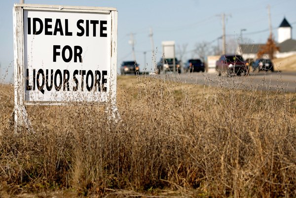 Motorists pass along West Walnut Street on Friday in Rogers past a sign promoting property for sale near the intersection with South 28th Street in Rogers. In November, Benton County voters approved retail alcohol sales in the county. 