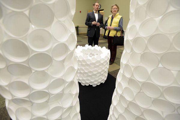 Stephen Coler, left, talks Friday about his sculptural arrangement made of foam cups with Gloria Southerland of Fayetteville on the first day of Coler’s Ikebana floral arrangement show at the Bentonville Public Library. 