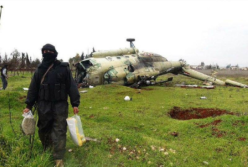 A Syrian rebel carries food Friday as he walks in front of a damaged helicopter at Taftanaz air base in northern Syria after the base was captured by rebel forces. This image was provided by the Edlib News Network and authenticated by The Associated Press. 