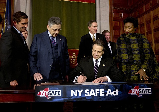 New York Gov. Andrew Cuomo signs a bill toughening gun laws in his state as leading lawmakers gather around Tuesday at the state Capitol in Albany. 