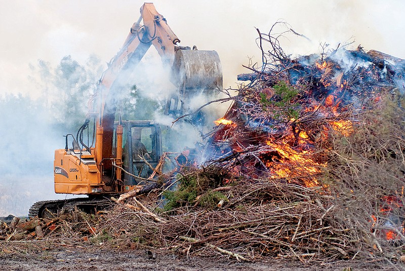 Brett Koder with the Saline County Road Department uses a track hoe to pile broken trees and limbs from the area’s recent winter storm onto a pile to burn.