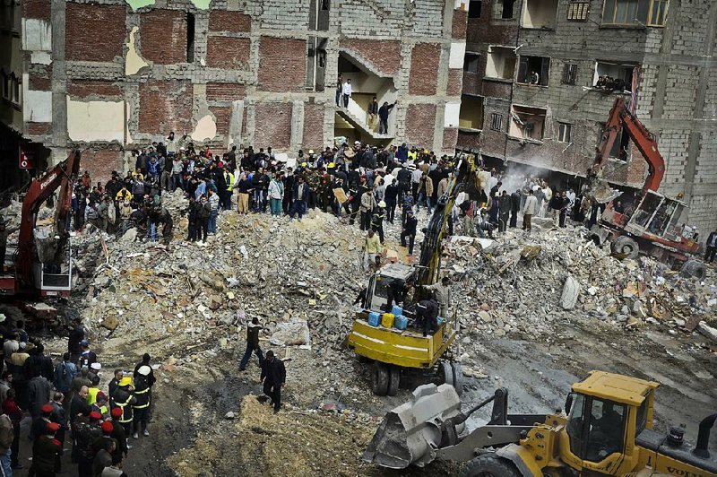 Egyptians stand in rubble after an eight story building collapsed in Alexandria, Egypt, Wednesday, Jan. 16, 2013. Egypt’s official MENA news agency says at least fourteen people have been killed. It was not immediately known what caused the building to collapse, but violations of building specifications have been blamed in the past for similar accidents. (AP Photo)