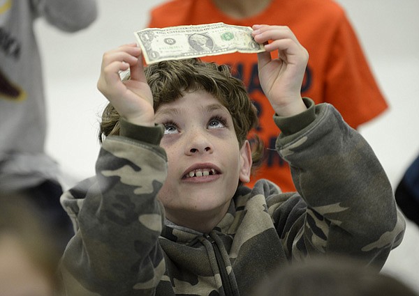 Gabriel Creasey, 9, checks out the $1 bill he received Friday while attending a program on saving money presented by representatives of Walmart’s Finance and Accounting Department at Elm Tree Elementary School in Bentonville. The Arkansas Kids Count program, sponsored by the Arkansas Society of Certified Public Accountants, teaches third- and fourth-graders the importance of saving money, spending wisely and setting financial goals. 