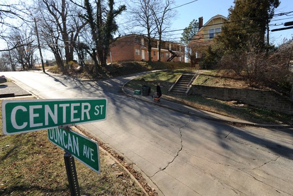 A pedestrian walks north Wednesday on Duncan Avenue to Center Street in Fayetteville past a house and small apartment building among several properties to be razed to make room for a planned five-story, 175-unit apartment complex approved Monday by Fayetteville’s Planning Commission. 