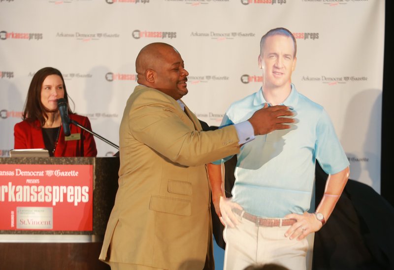 Arkansas Democrat-Gazette events manager Tabitha Cunningham, left, watches as Keith Jackson unveils a cutout of Peyton Manning, who will be the keynote speaker of the All Arkansas Preps awards banquet.