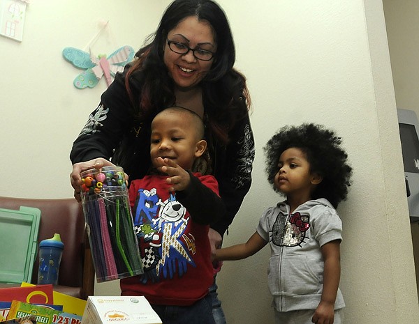 Kenneth Davis, 3, plays with one of the gifts he received Tuesday for being the 100,000th patient at the Community Clinic in Rogers. Him mom, Gisela Davis, and his sister, Marcela Davis, got in on the fun. 