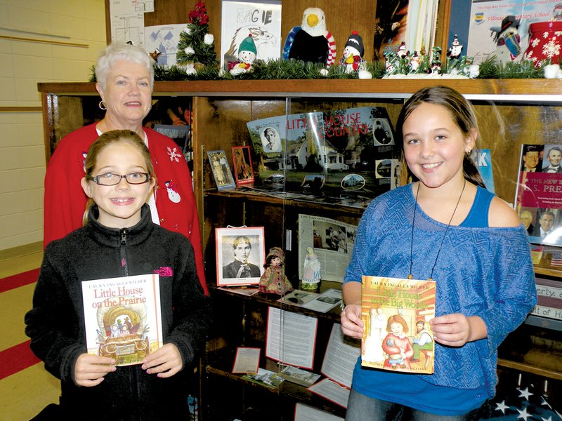 Taking a look at some of the items honoring American author Laura Ingalls Wilder, are, in the back, Carolyn Frazier, a retired second-grade teacher who taught at Vilonia Elementary School and one of the organizers of the display at the school’s library; and front, from the left, Evy McKissack and Janie Gentry, fourth-graders at the elementary school and readers of Wilder’s Little House books.