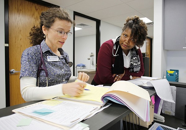 Marr-Lynn Flory, left, and LaTure Hicks, both advanced practical nurses, discuss the care of a patient at the nurses station in the new location of the Northwest Arkansas Free Health Clinic, 1100 N. Woolsey Ave. in Fayetteville. Changes to federal health care laws will require everyone to either obtain health care insurance or pay a penalty on their federal income tax returns beginning in 2014. 