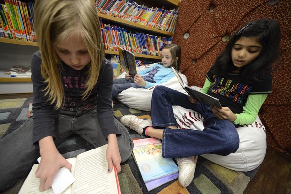 Emily Hornick, 8, from left, Madison Rector, 8, and Neha Soman, 9, all third-graders, read books they checked out Wednesday during their class’ weekly visit to their school’s library at Apple Glen Elementary School in Bentonville. 