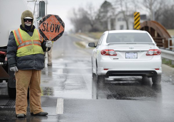 Mark Glover with Decco Contractors Paving handles traffic control Wednesday as crews work to level sections of pavement on Southwest ‘I’ Street in Bentonville. The improved stretch of road between Southwest 14th Street and Southwest Regional Airport Boulevard officially opened Jan. 22. 