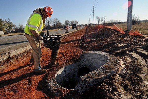 David Einsele works Friday to compact dirt around new drainage that has been laid as work begins to widen Arkansas 102 from Greenhouse Road to Centerton. 