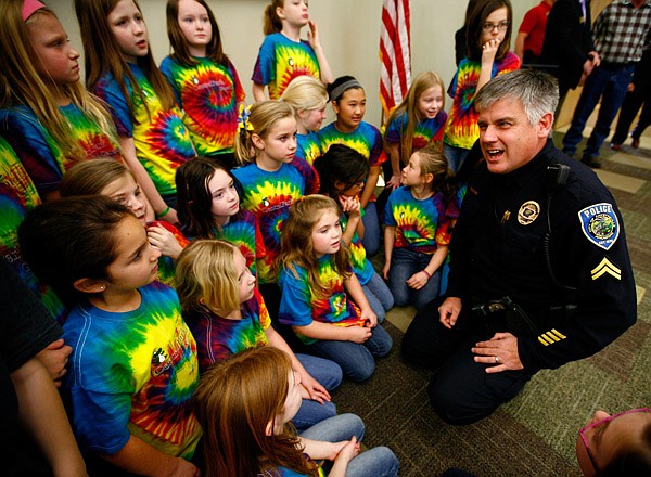 Fayetteville Police Cpl. David Williams talks Wednesday with members of the Gator Choir from Central Park Elementary School before a ceremony at the Bentonville Public Library. During the ceremony, four area Rotary Clubs presented checks totaling $44,500 for the National Child Protection Center at NorthWest Arkansas Community College in Bentonville. The choir performed the national anthem. 