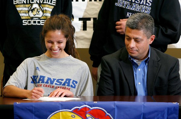 Tayler Estrada signs her letter of intent on Wednesday as her father, Doug Estrada, watches inside the Tiger Athletic Complex at Bentonville High. Tayler Estrada signed to play soccer for University of Kansas. 