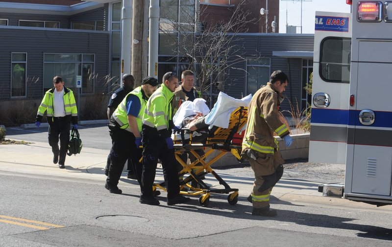 Emergency personnel work with University Police Department officers Friday to load a patient into an ambulance after a report of a man who suffered an accidental self-inflicted gunshot wound to his hand at the KUAF studio.