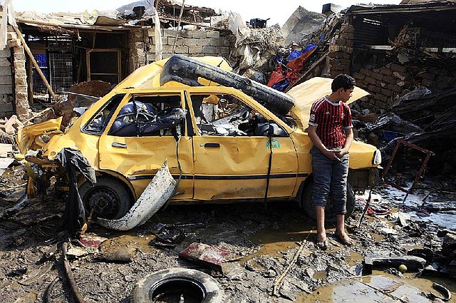 An Iraqi boy stands near a destroyed car Friday at the scene of a car-bomb attack in Baghdad’s northern Kazimyah neighborhood. 