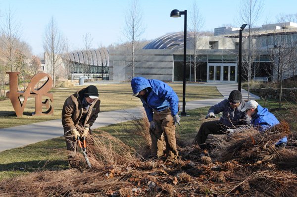 William Aguilar, from right, Fernando Silza, Josh Erickson and Brian Batchelor work Friday to cut bluestem grass in one of the gardens outside the south entrance to Crystal Bridges Museum of American Art in Bentonville. The men work for Crystal Bridges’ trail and ground staff that maintains the gardens and trails around the museum. 