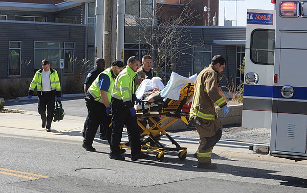 Fayetteville emergency personnel work with University Police Department officers Friday to load a patient into an ambulance after a report of a man who suffered an accidental self-inflicted gunshot wound to his hand at the KUAF studio on School Avenue in Fayetteville. 