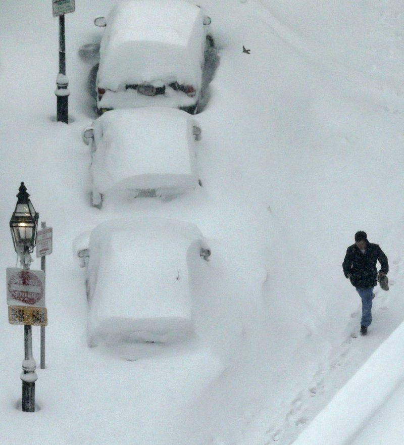 A man walks past snow covered cars in the South End neighborhood of Boston, Saturday, Feb. 9, 2013. The Boston area received about two feet of snow from a winter storm.