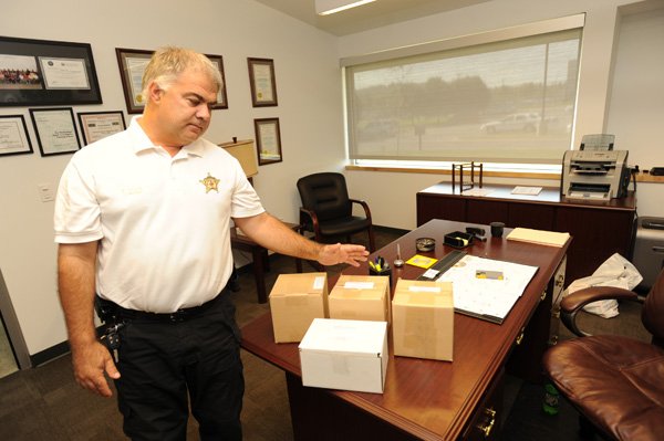 Roger Morris, Washington County coroner, shows one of a few unclaimed cremated human remains that he stores at his office Aug. 15 in Fayetteville. Morris received an extra $20,000 from the Quorum Court to do spot checks on deaths at nursing homes this year.