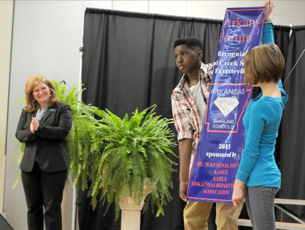 Zoe Reif, 12, from right, and Maynard Valley, 13, both students at Owl Creek School, hold a banner Tuesday recognizing the fifth, sixth and seventh grades as a 2013 Arkansas Diamond School to Watch as school principal Kristen Champion looks on during a ceremony at the school in Fayetteville. The national and state recognition is for advancing student test scores. Previously the school was on the needs improvement list.