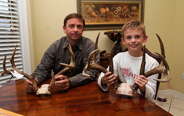 Eight-year-old Davis Stephens of Fayetteville, right, scored a Triple Trophy Award this deer season while hunting with his dad, Tracy Stephens, left. The award, from the Arkansas Game & Fish Commission, is presented to hunters who harvest a deer by all three methods — archery, muzzle-loader and modern gun. The pair show antlers from two of the deer Davis killed this season. 