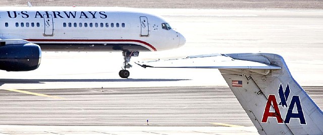 FILE - In this Feb. 7, 2013 file photo, a US Airways jet taxis past an American Airlines jet parked at the gate at Sky Harbor International Airport in Phoenix. The merger of US Airways and American Airlines has given birth to a mega airline with more passengers than any other in the world. (AP Photo/The Arizona Republic,Tom Tinkle, File)  MARICOPA COUNTY OUT; MAGS OUT;