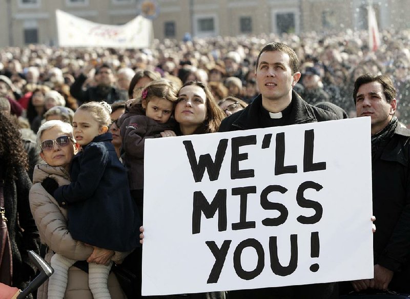 A priest displays a placard in St. Peter’s Square at the Vatican as he follows Pope Benedict XVI reciting the Angelus prayer Sunday. The pope blessed the faithful from his window overlooking St. Peter’s Square for the first time since announcing his resignation. 