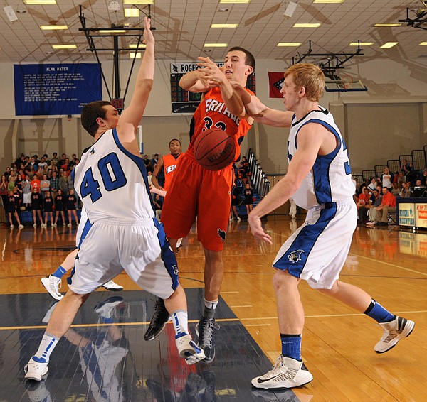 Luke Fryauf,
center, Rogers Heritage, is fouled under the net by Rogers High’s Zach Jones, right, on Tuesday at King Arena in Rogers. 