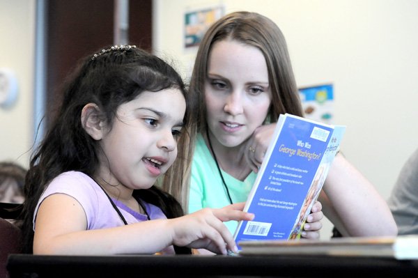 Anna Bever, right, child care coordinator with the Jones Center’s after-school program, reads a book Tuesday with Soyla Rodriguez, 7, at the center in Springdale.