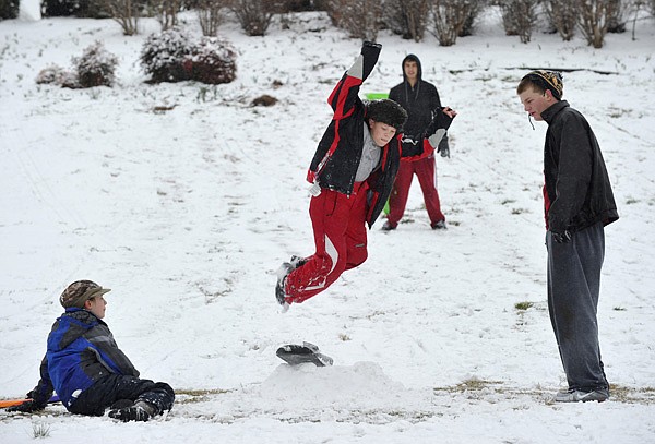 Anna Beth La Tour, 14 of Fayetteville, left, and University of Arkansas student Mitchell Loewen from Hawaii, watch Wednesday as Luke La Tour, 11 of Fayetteville catches air while riding a snowboard down the hill just north of Reynolds Razorback Stadium in Fayetteville. Fayetteville schools closed early after a cold front moved across the area covering the area with a light layer of snow. More photos online at photos.nwaonline.com.